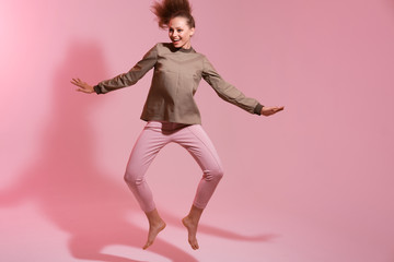 Full length portrait of a happy young woman celebrating success while jumping isolated over pink background. Life people energy concept