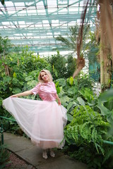 beautiful white long hair girl in a tropical garden walks and dances in a light tulle pink skirt