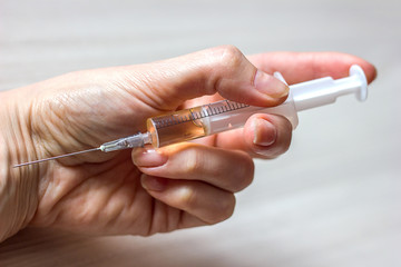 syringe with an injection in a female hand close-up, drug addiction topic, treatment of diseases,...