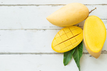 Top view mangos with sliced and green leaves on wooden table.