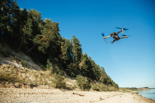 Compact Drone flying over the forest landscape against blue sky. Flying remote camera.