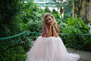 Obraz na płótnie Canvas beautiful white long hair girl in a tropical garden in a light tulle pink skirt
