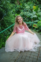 Obraz na płótnie Canvas beautiful white long hair girl in a tropical garden in a light tulle pink skirt