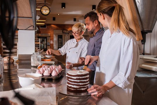 Group of workers in uniform decorating desserts in modern manufacturing.