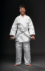 a teenager dressed in martial arts clothing poses and having fun on a dark gray background, a sports concept