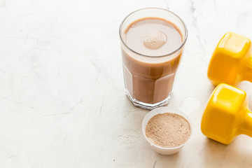 Protein shake in glass near dumbbells on white background copy space