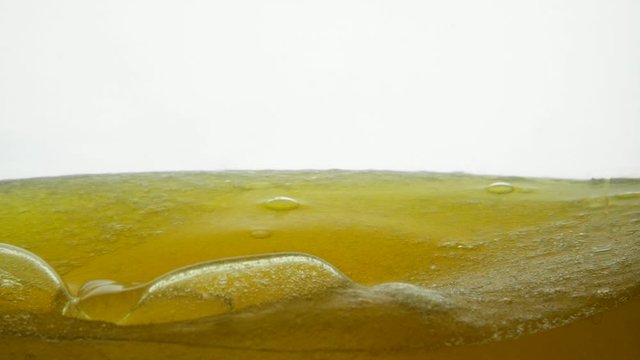 Golden liquid with bubbles and droplets of air on the surface. Corn oil is poured with argan oil in a transparent container. Close shot of sesame oil and golden black cumin oil on a white background.