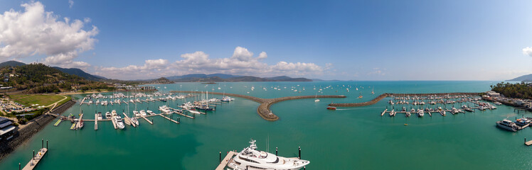 Panoramic marina town aerial. Airlie beach waterfront aerial view. Dramatic DRONE view from above. Marina town with yachts and boats in sea water. Mountain landscape background. Whitsundays Islands