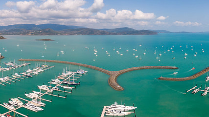 Panoramic marina town aerial. Airlie beach waterfront aerial view. Dramatic DRONE view from above. Marina town with yachts and boats in sea water. Mountain landscape background. Whitsundays Islands
