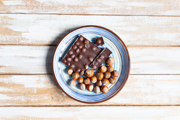 Black chocolate bar with hazelnuts  in bowl on wooden background