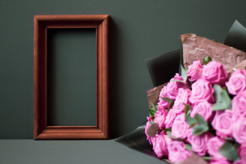 Flower arrangement. Pink flowers, wooden brown photo frame on pastel green background, copy space