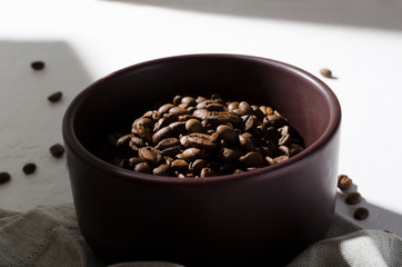 Closeup of roasted coffee beans in the brwn bowl standing on the white table, morning light from window