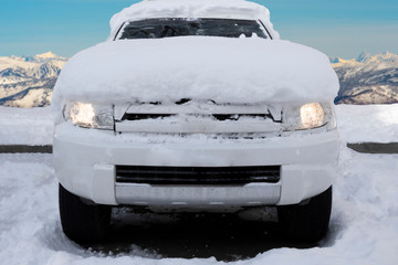 Car covered with snow after snowfall with mountains background. SUV in mountains after  blizzard.