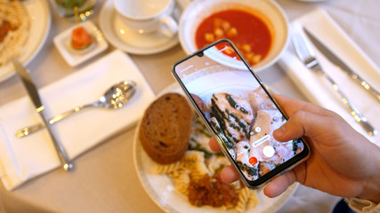 Hands using smartphone taking photos of chicken pasta with tomato coup and piece of bread