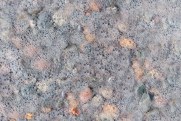 Pebbles covered with seafoam background. Rocks and bubbles background. Sea foam background.