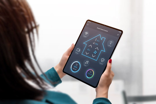 Smart home central control system on tablet display. Concept app design in woman hands. Home interior in background