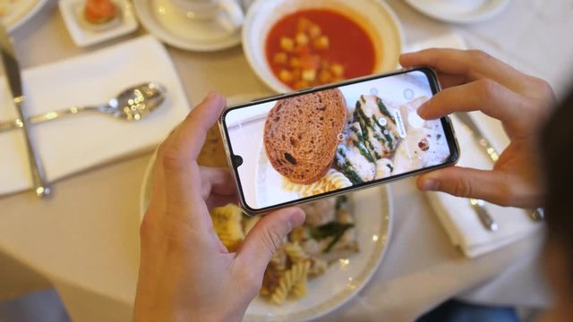 Hands using smartphone taking photos of chicken pasta with tomato coup and slice of bread