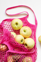 Pink mesh shopping bag with fresh apples on white wooden background