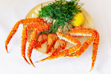 Shrimp, crab, lemon and greens on a plate on a white background.