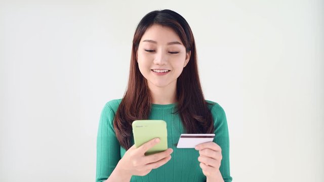 Happy smiling young girl holding credit card and shopping online through smartphone isolated over white