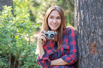 Asian girl with an old camera in a forest. Girl in checkered shirt and blue jeans taking photo on an old camera. Vintage style...