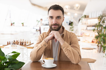 Fototapeta na wymiar young bearded attractive man drinks coffee during his lunch break in the cafe, positive vibes