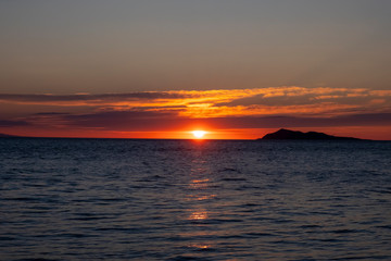 Beautiful sea sunset with island silhouette. Orange sunrise over the sea.