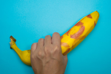 Hand holding banana with red lipstick on it on a blue background