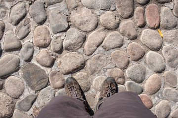 Man's feet on rock cobblestone road...Man in shorts and hiking boots is  standind on stone pavement.