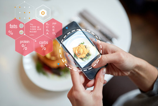 food, new nordic cuisine, technology, eating and people concept - close up of hands with breaded fish fillet on smartphone screen and nutritional value chart at restaurant
