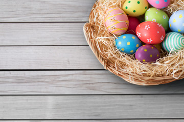 easter, holidays and traditions concept - close up of colored eggs in wicker basket over grey wooden boards background