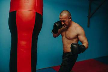 Male boxer training with punching bag in dark sports hall.Male boxer as exercise for the big fight....