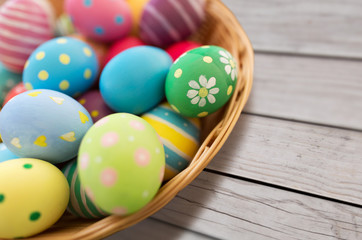 Fototapeta na wymiar easter, holidays and tradition concept - close up of colored eggs in wicker basket on grey wooden boards background