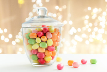 food, confectionery and sweets concept - glass jar with colorful candy drops over festive lights background