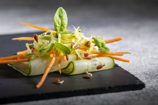 Vegetarian paleo diet cucumber slice with carrots, green radish, microgrin sprouts of radish and sunflower, wheat and flax sprouts. On black background. Macro.