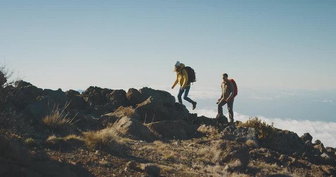 Young adventurous backpackers hiking on a mountain top above the clouds, active couple walking in the wilderness together