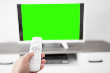 Hand holding TV remote controller with a modern television set. © astrosystem
