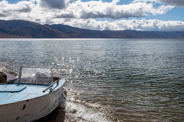 Old fishing boat on the lake with cloudy sky and mountains background.