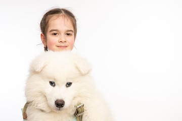 Close up photo of the confident beautiful child and white cute ssamoyed puppy, both looking at the camera isolated over white background