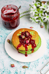 Green pancakes with matcha powder with red jam on light background,top view
