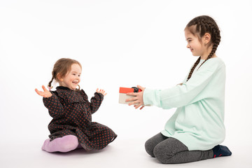 Beautiful teen girl with pigtails gives present box to her little excited sister in red pea dress, Happy New Year concept