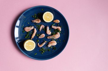Boiled shrimps, sea salt, milled pepper, greenery, lemon on blue plate on pink background