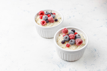 Rice pudding with frozen blueberries and raspberries in white bowl