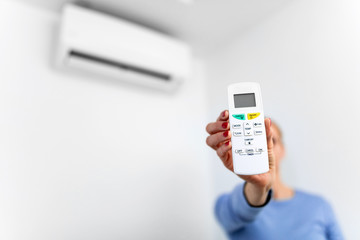 Woman holding a remote of a modern airconditioner unit at home.