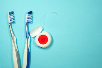 Closeup of two new plastic toothbrushes and dental floss on a blue background. Dental heathcare concept.