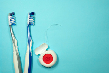 Closeup of two new plastic toothbrushes and dental floss on a blue background. Dental heathcare concept.
