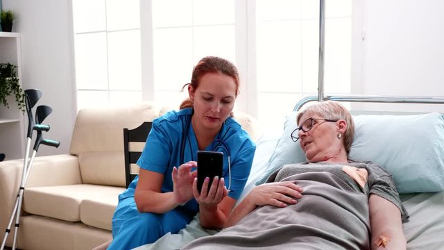 Female nurse helping old woman to use smartphone