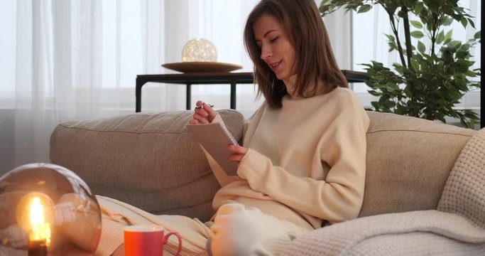 Thoughtful woman coming up with a good idea while writing in notepad at home
