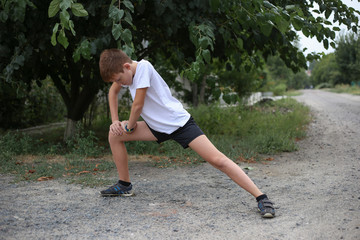 Teenager in white t-shirt does stretching legs in the park