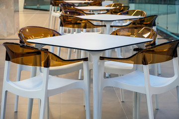 Many orange plastic chairs and a white tables on food court in mall.